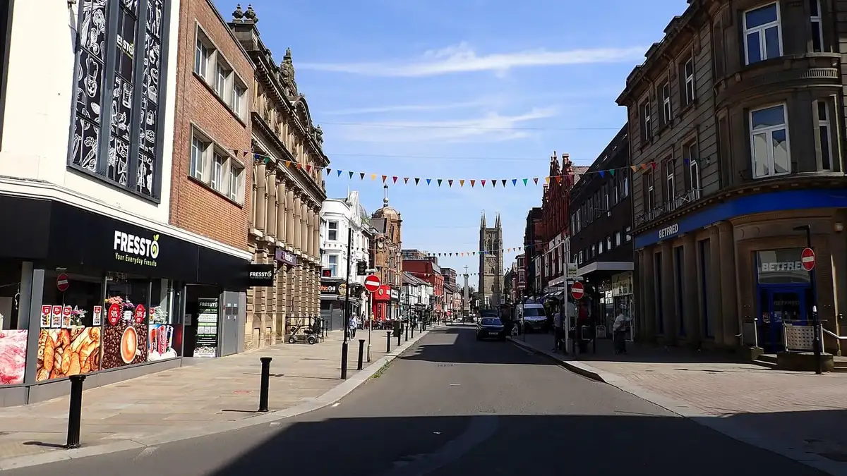 Shops and Victorian buildings along Deansgate, Bolton, under a blue sky