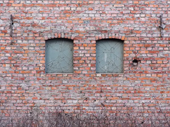 Two windows with cracked glass panes in an old red-brick wall