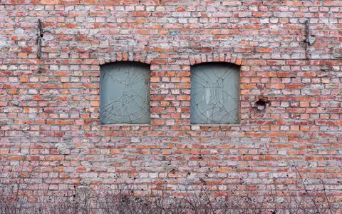 Two windows with cracked glass panes in an old red-brick wall