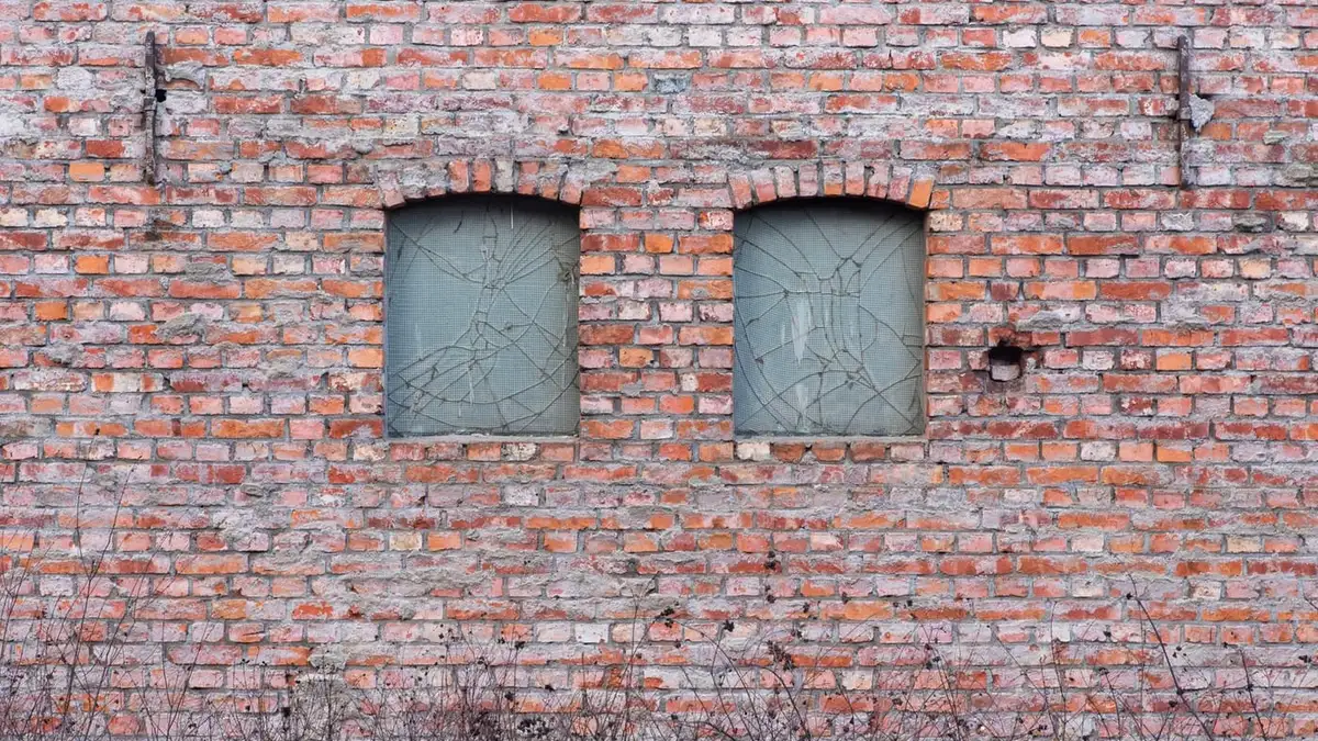 Two windows with cracked glass panes in an old red-brick wall