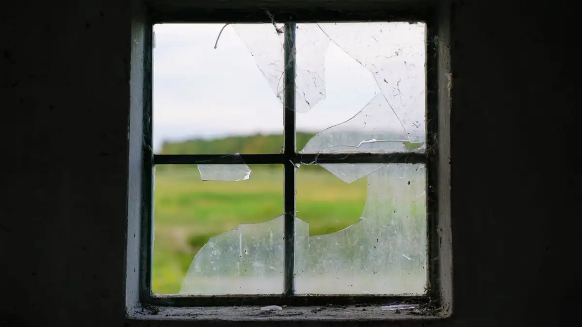 Wooden window frame with shattered glass panes, green fields beyond