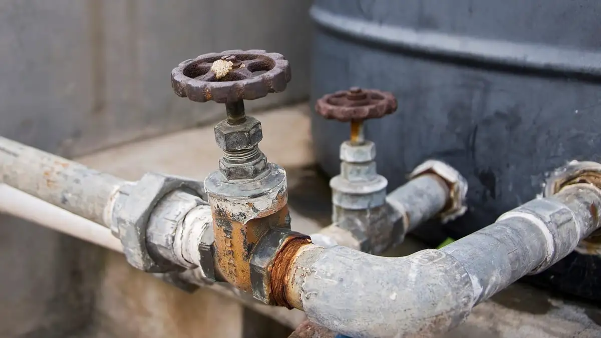 Two stopcock valves with red wheel handles on galvanised water pipes
