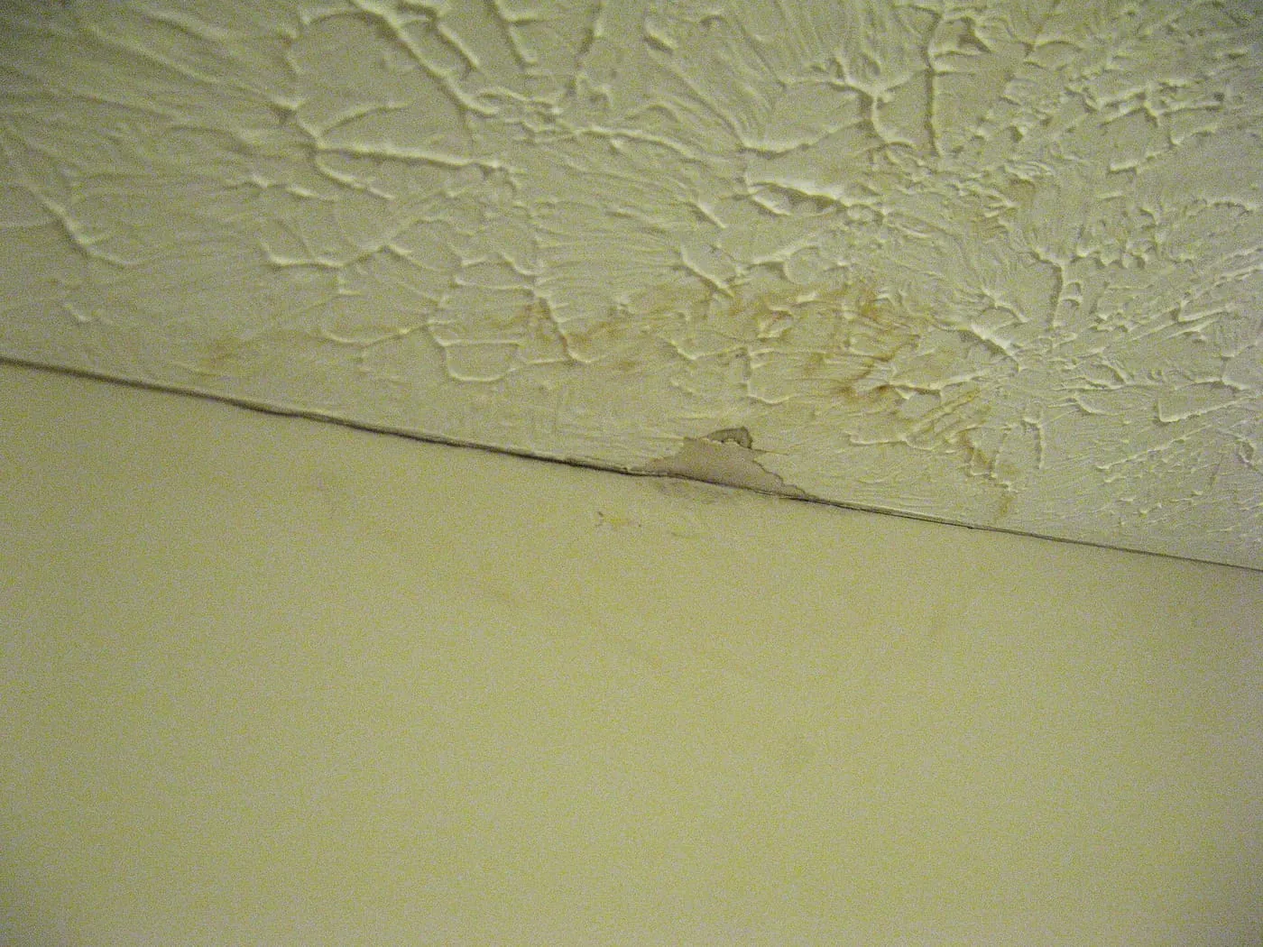 Brown water stain on a textured ceiling caused by a rain leak