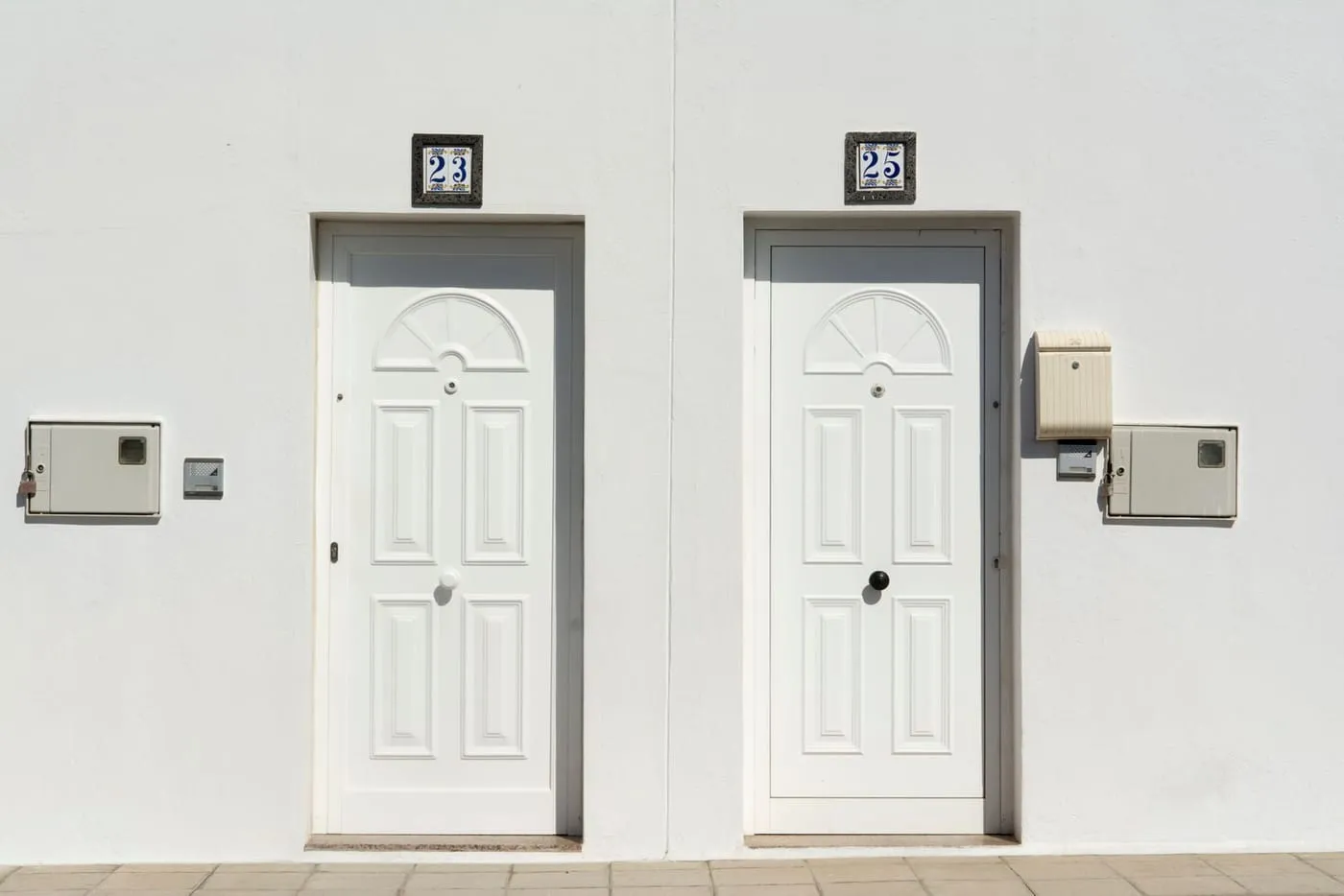 Two white panelled front doors with handles and keyholes on a white wall