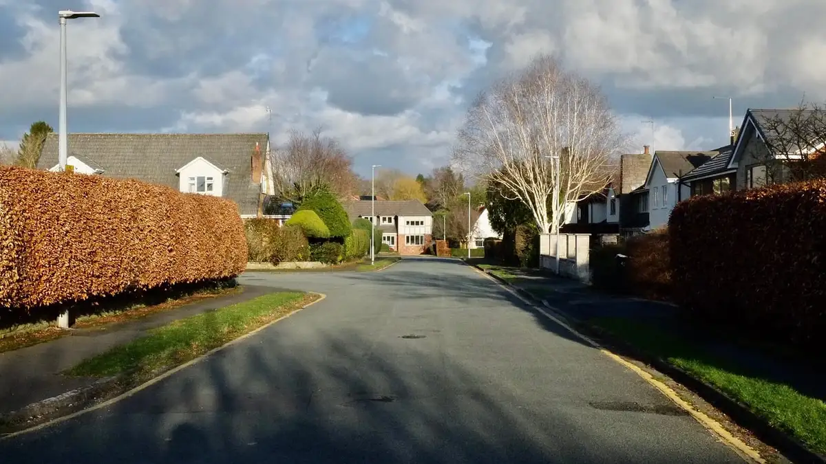 Curving residential road lined with hedges and houses in Wilmslow, Cheshire