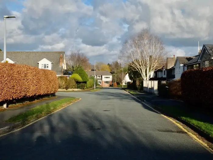 Curving residential road lined with hedges and houses in Wilmslow, Cheshire